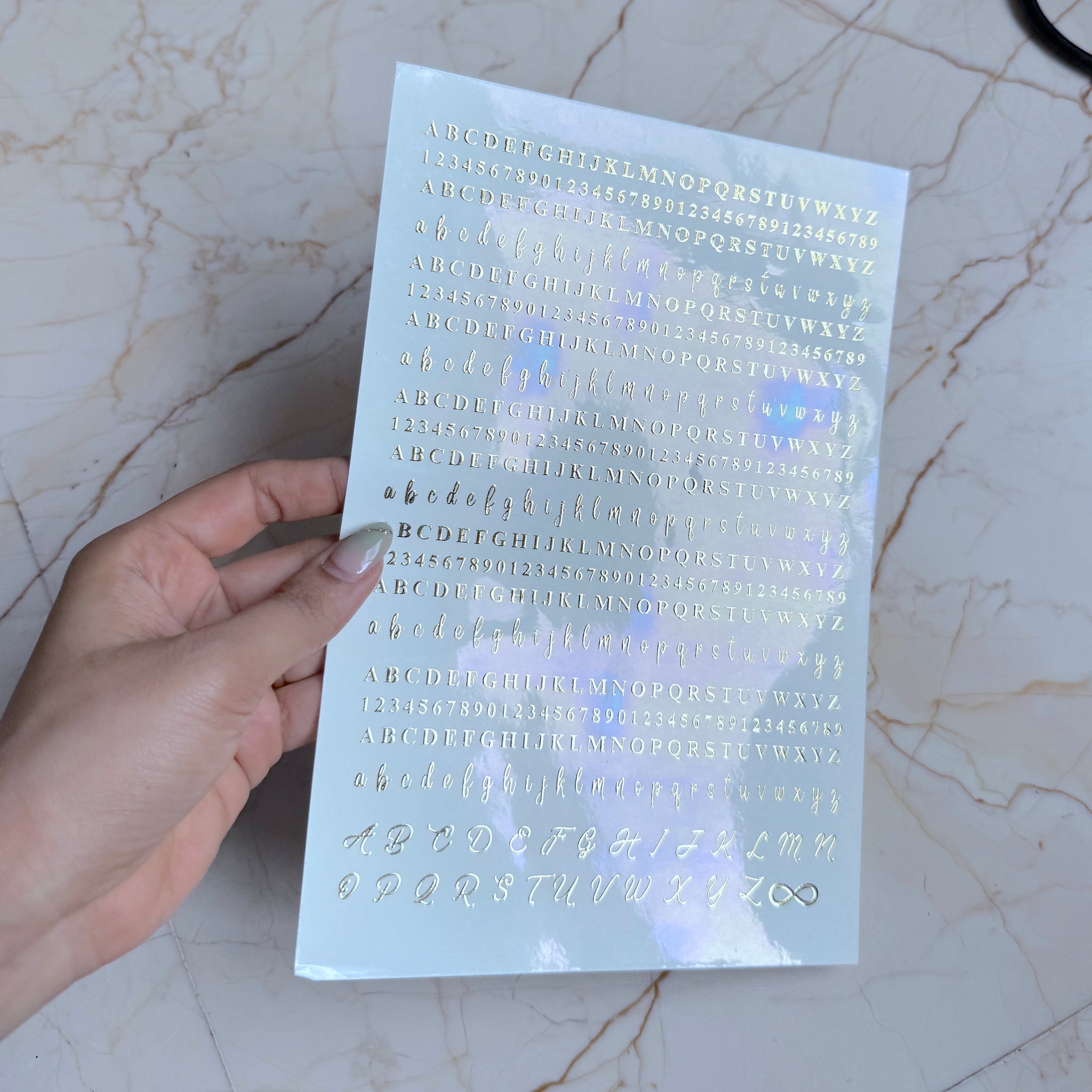 Hand holding a transparent sheet with embossed letters and numbers on a marble surface