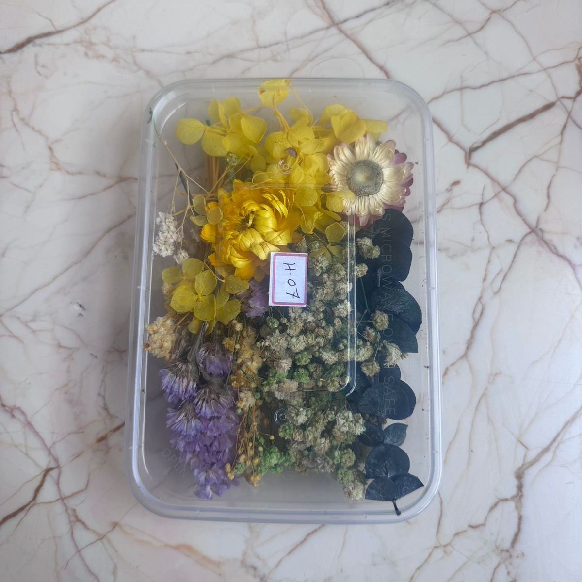 Assorted dried flowers in a clear plastic container on a marble surface