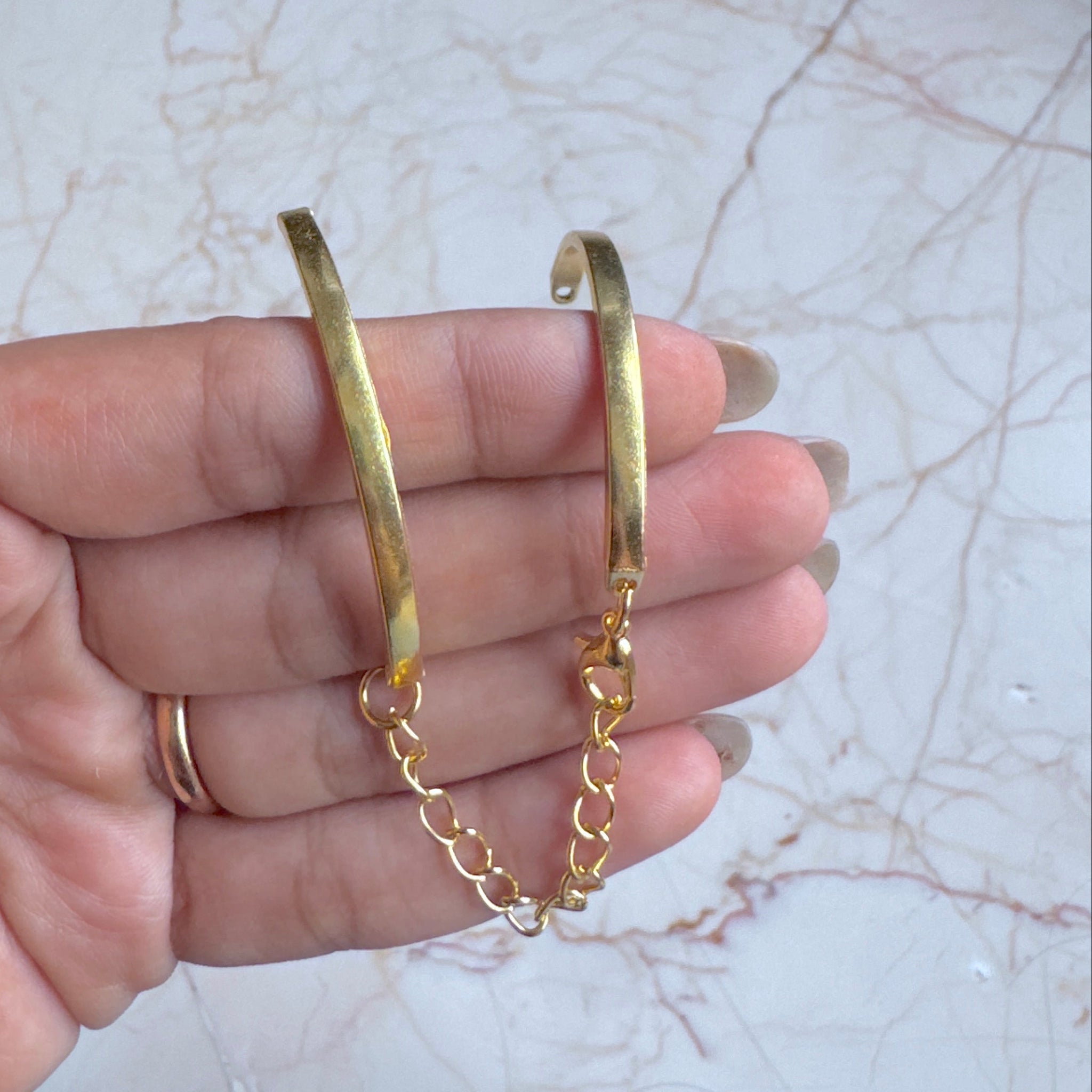 Gold hoop earrings held in a hand against a marble surface