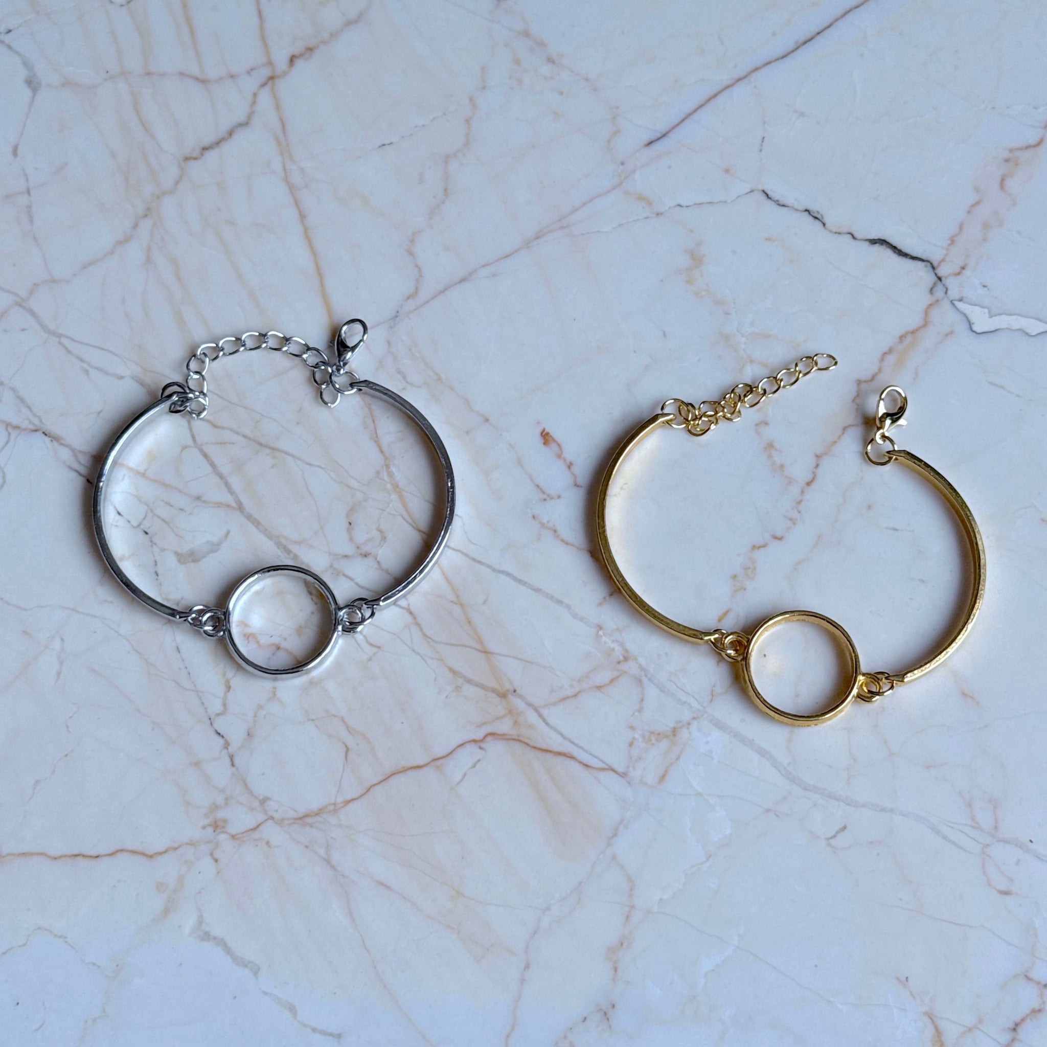 Two bracelets, one silver and one gold, on a marble surface