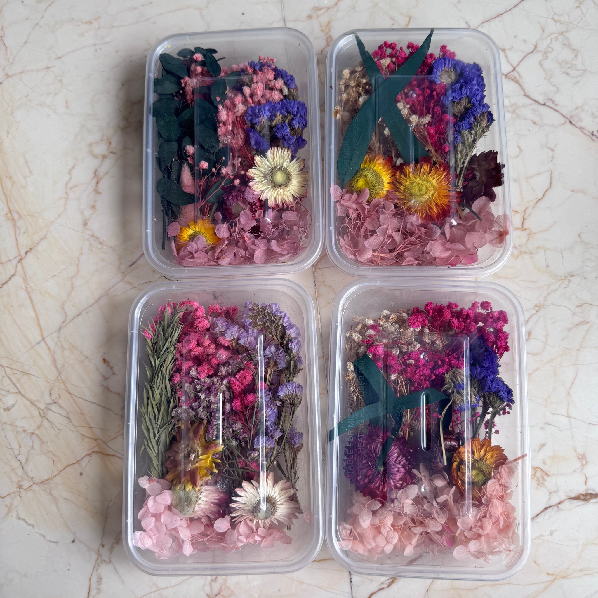 Four containers with dried flowers on a marble surface