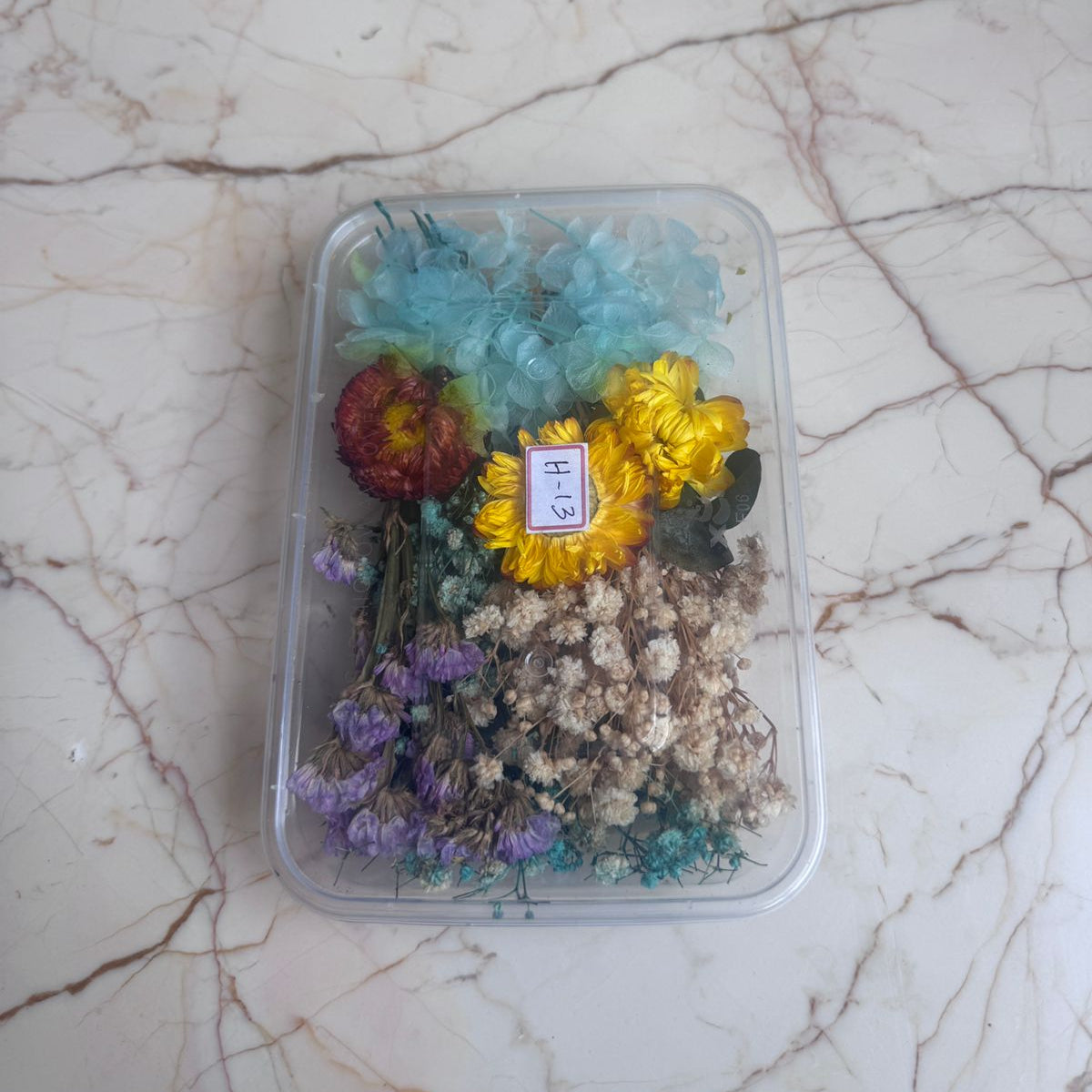 Assorted dried flowers in a clear container on a marble surface