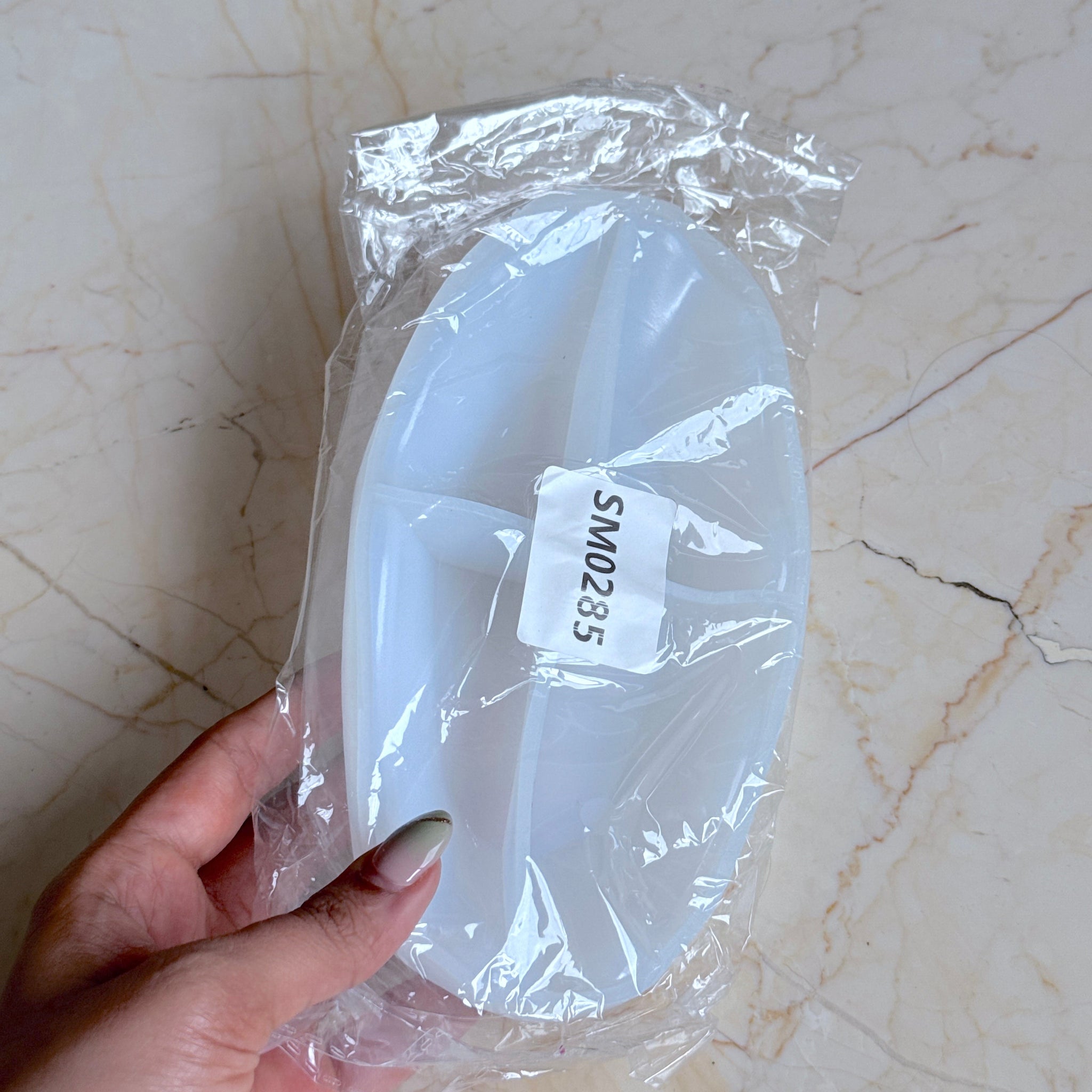 Silicone mold in clear plastic packaging held by a hand on a marble surface