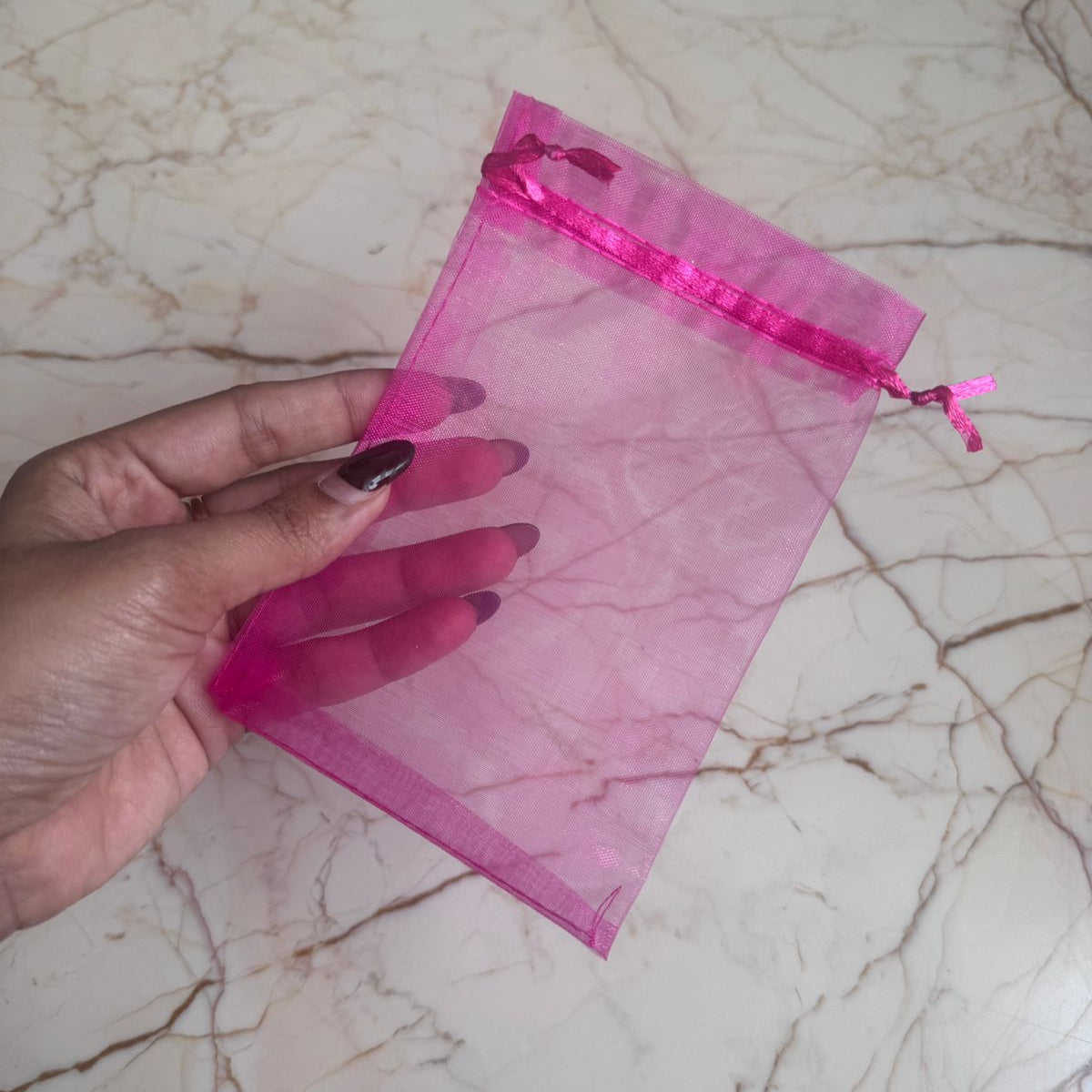 Hand holding a pink sheer bag on a marble surface