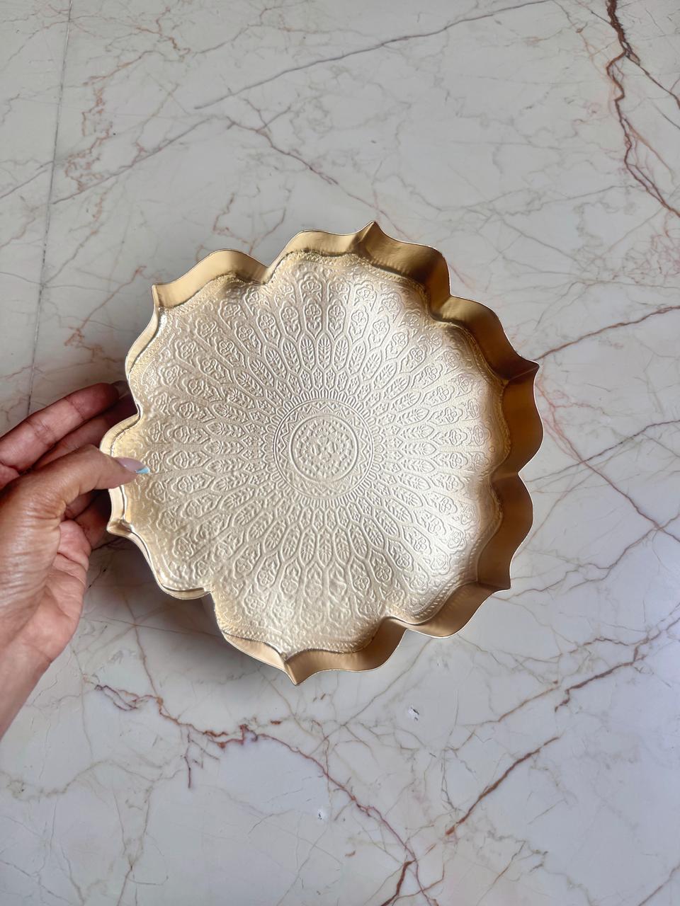 Decorative gold plate held by a hand on a marble surface
