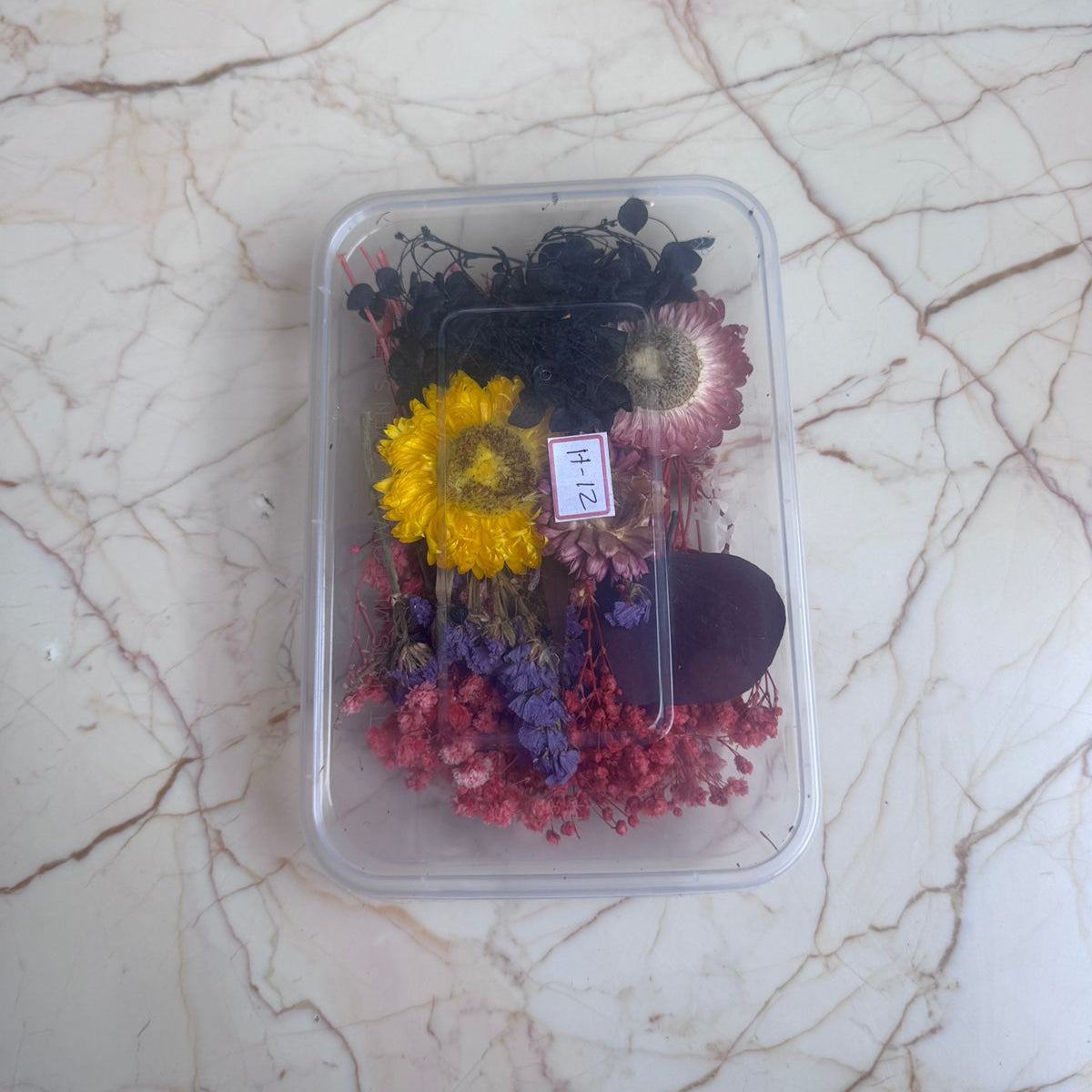 Assorted dried flowers in a clear plastic container on a marble surface
