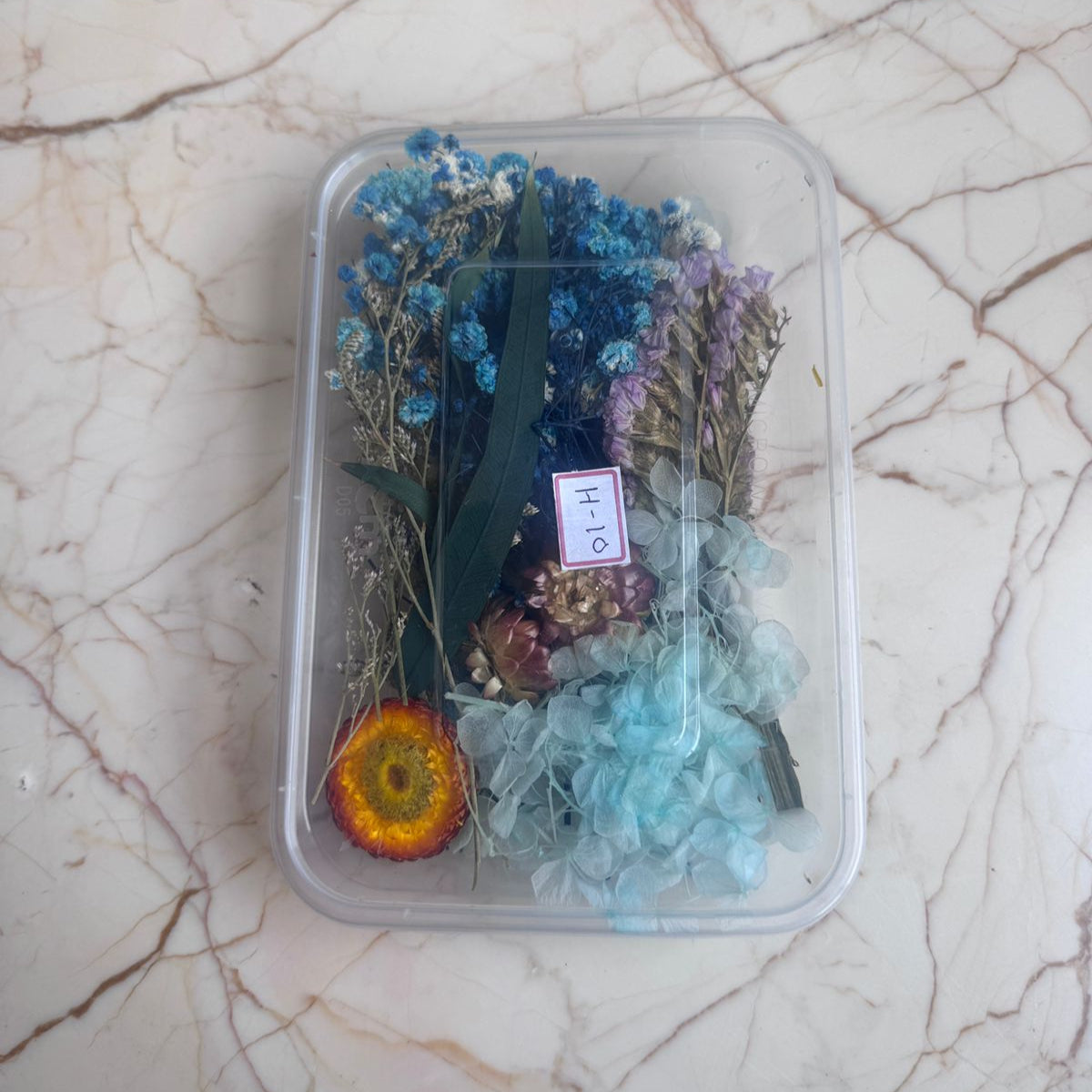 Clear plastic container with dried flowers on a marble surface