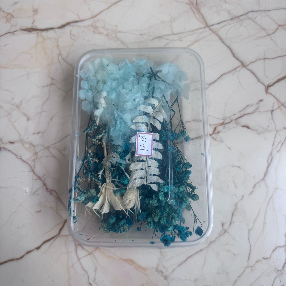 Clear plastic container with blue and white decorative items on a marble surface