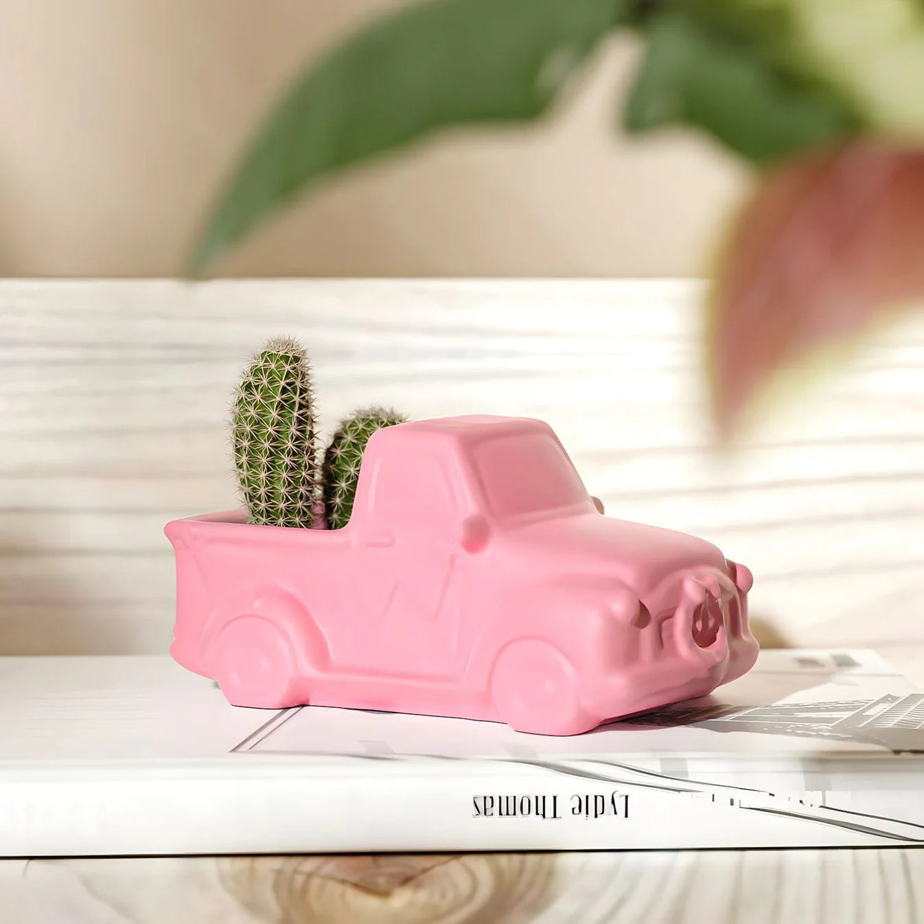 Pink truck-shaped planter with a cactus on a wooden surface