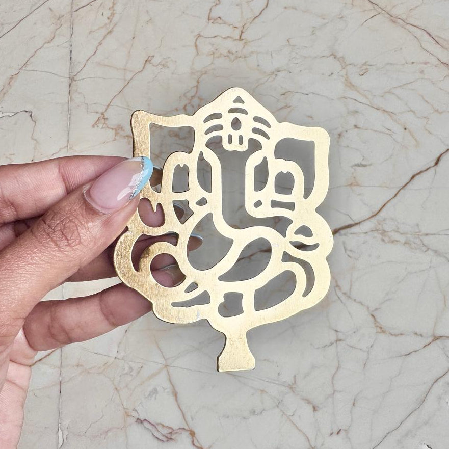 Gold decorative item shaped like a deity figure held by a hand on a marble surface