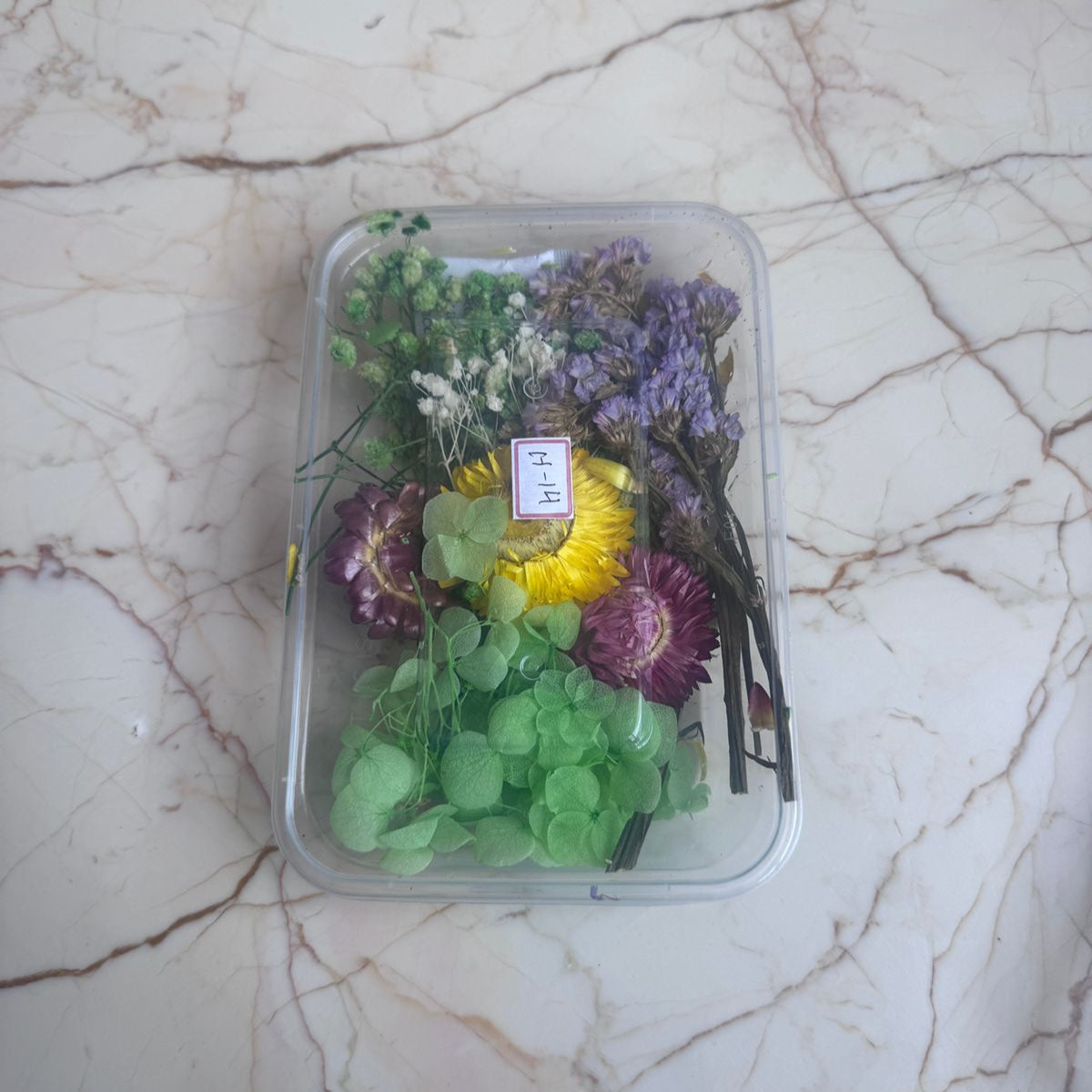 Assorted flowers in a clear plastic container on a marble surface
