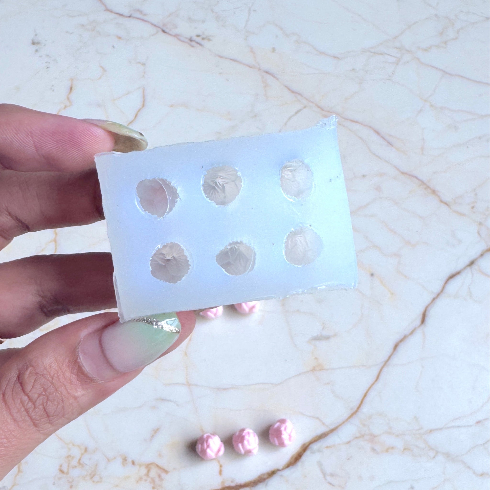 Hand holding a white plastic grid with pink earrings on a marble surface