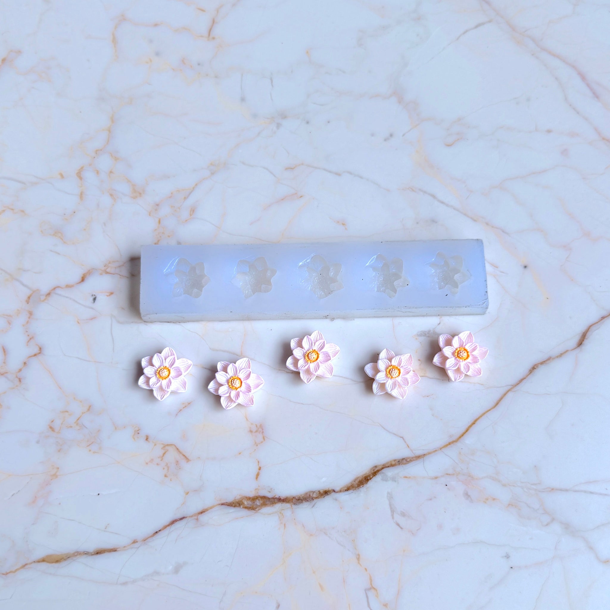 Flower-shaped earrings on a marble surface with a ruler for scale.