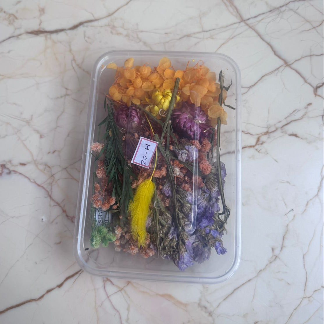 Assorted dried flowers in a clear plastic container on a marble surface