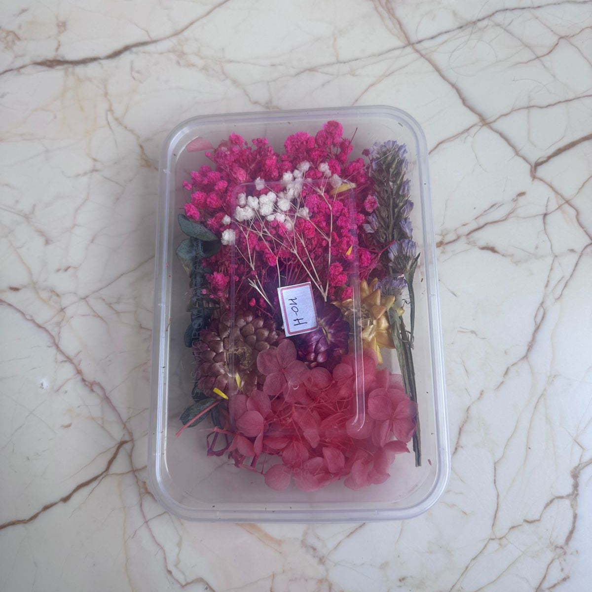 Container of dried flowers on a marble surface