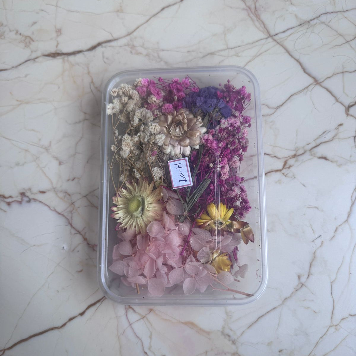 Container filled with dried flowers on a marble surface