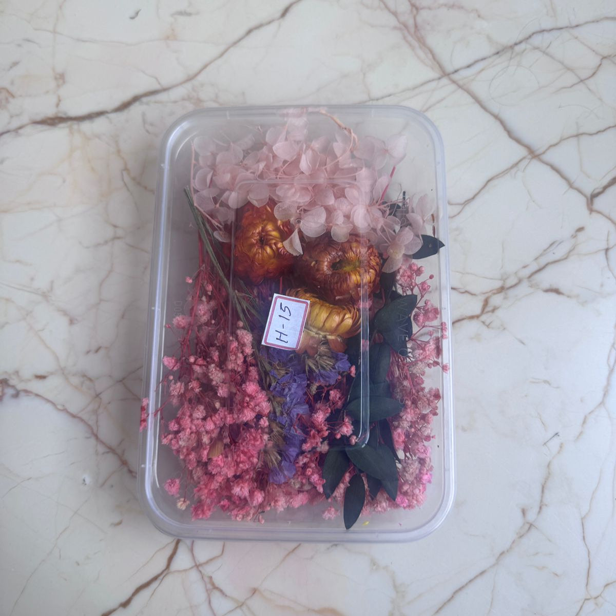 Clear container with dried flowers and a butterfly on a marble surface