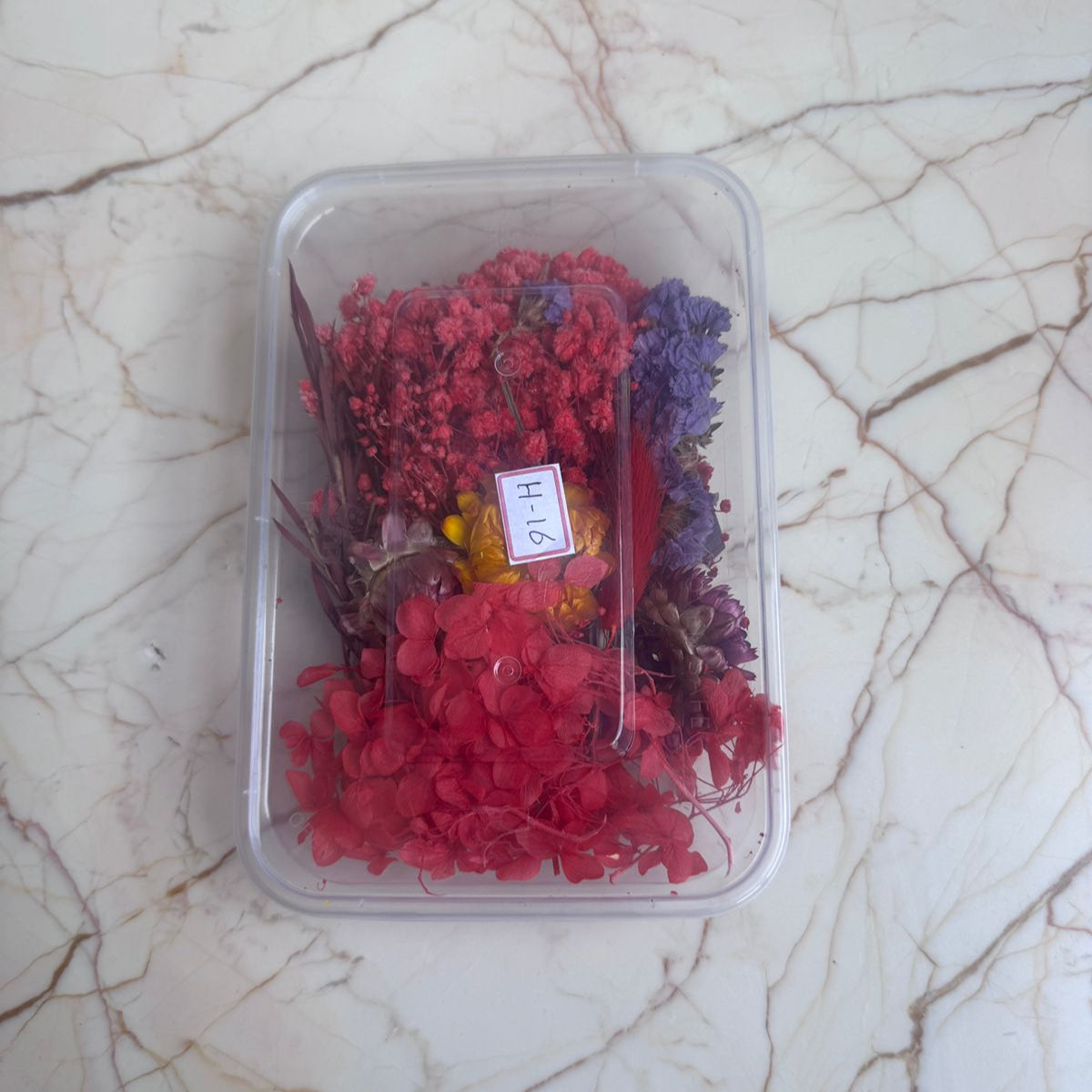 Clear container with red and purple dried flowers on a marble surface