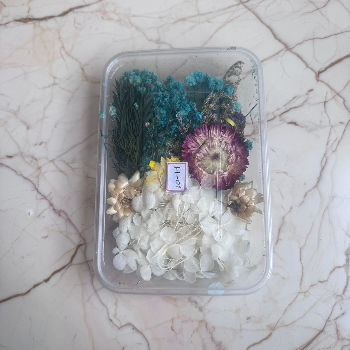 Clear container with dried flowers and plants on a marble surface